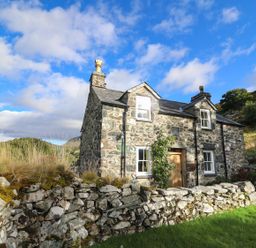 A stone house with a wooden door and windows surrounded by a stone wall and grass at Tyn Y Graig in Fairbourne