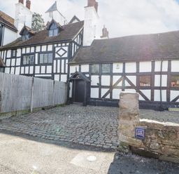 A cobblestone driveway and timber framed buildings with white and black walls at Wyre Court Cottage in Bewdley