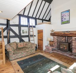 A living room with patterned sofas wooden stairs a brick fireplace and a framed poster at Wyre Court Cottage in Bewdley