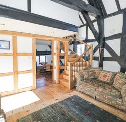 A living room with patterned sofas a wooden staircase and exposed wooden beams at Wyre Court Cottage in Bewdley