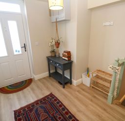 An entryway with a white door a dark small table with drawers a plant a shoe rack and a sign asking to remove shoes at Cottage Annex in Constantine