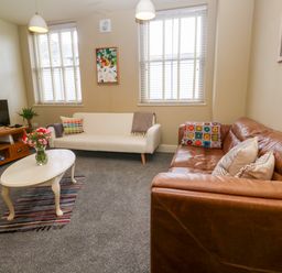 A living room with two sofas a coffee table with flowers and a television on a wooden stand at Cottage Annex in Constantine