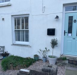 The exterior of a white house with a light blue door numbered 44 a black mailbox a bench and several potted plants in front of the Cottage Annex in Constantine