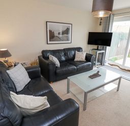 A living room with two black leather sofas a glass coffee table a lamp and a television by a sliding glass door at Sea Shore in Seahouses