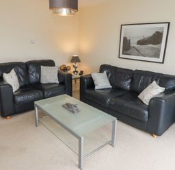 A living room with two black leather sofas a glass coffee table and a framed photo on the wall at Sea Shore in Seahouses