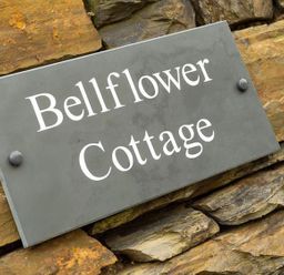 A gray sign with white text reading Bellflower Cottage mounted on a stone wall at Bellflower Cottage in Windermere