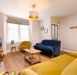 A living room with a blue sofa a yellow armchair a wooden coffee table and a television at Bellflower Cottage in Windermere