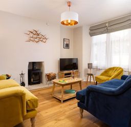 A living room with yellow and blue sofas a wooden coffee table a television and a fireplace at Bellflower Cottage in Windermere