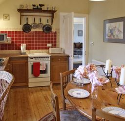 A kitchen with wooden cabinets red tiled backsplash stove and a dining table set with plates candles and napkins at Bank View in Chirnside