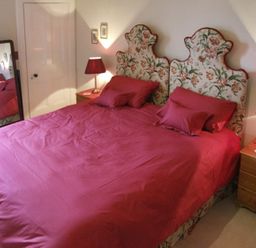A bedroom with a double bed with a red bedspread and floral headboards two bedside tables with lamps and a standing mirror at Bank View in Chirnside