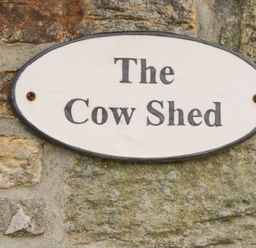 An oval sign with The Cow Shed mounted on a stone wall at Cowshed in Normanby near Flyingthorpe