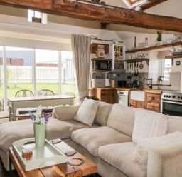 A living area with a beige sofa a wooden coffee table a dining table and a kitchen with wooden cabinets at Cowshed Normanby near Flyingthorpe
