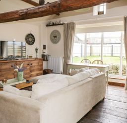 A living room with a white couch a wooden TV cabinet and a dining table near glass doors at Cowshed Normanby near Flyingthorpe