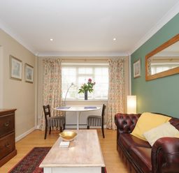 A living room with a brown leather sofa yellow cushions a wooden coffee table a small dining table with two chairs and a wooden dresser at Alway in Lifton