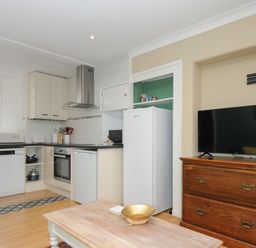 A kitchen with white cabinets dishwasher oven fridge and a wooden chest with a television at Alway Lifton