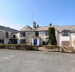 A historic building with arched windows and a blue door with a gravel parking area in front at Alway in Lifton