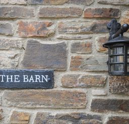 A stone wall with a black lantern and a sign that reads The Barn at The Barn in Lifton
