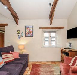 A living room with a purple sofa and a red armchair a wooden cabinet with a wall mounted TV and wooden ceiling beams at The Barn in Lifton