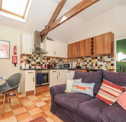 A kitchen with tiled backsplash white and wood cabinets and a purple sofa with cushions at The Barn in Lifton