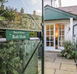 An entrance gate with a green sign reading Beech House Bolt Hole opening to a path leading to a white house with glass doors at The Bolt Hole in Kendal