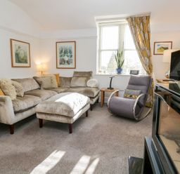 A living room with a beige sofa and a gray armchair near a window with yellow curtains at The Bolt Hole in Kendal