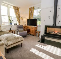 A living room with a sofa and armchair a television on a wooden cabinet and a fireplace at The Bolt Hole in Kendal