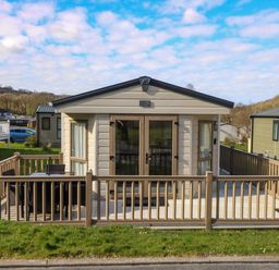 A beige mobile home with a wooden deck and outdoor furniture surrounded by a fence at 98 The Heron in New Quay