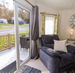 A living room with a large armchair a sideboard with a clock on the wall and sliding glass doors leading to a patio at 98 The Heron in New Quay