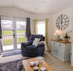 A living room with an armchair next to glass doors and a cabinet with a clock on the wall at 98 The Heron in New Quay