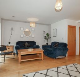 A living room with two blue sofas a wooden coffee table a black chair and wooden flooring at Treburgett Porthtowan