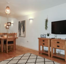 A dining area with wooden table and chairs and a wall-mounted television above two wooden cabinets at Treburgett in Porthtowan