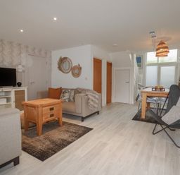 A living room with a television on a cabinet a beige sofa orange cushion and wood table at Trenethick in Porthtowan