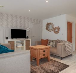 A living room with two sofas a wooden table a television on a cabinet and circular wall mirrors at Trenethick in Porthtowan