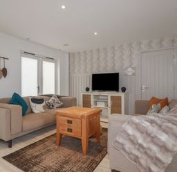 A living room with two beige sofas a wooden coffee table a rug and a television on a cabinet at Trenethick in Porthtowan