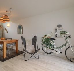 A dining area with wooden table and chairs next to a butterfly chair and a white bicycle adorned with flowers at Trenethick in Porthtowan