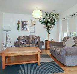 A living room with two striped sofas a wooden coffee table a floor lamp wall decorations and a large plant at Tregullan in Porthtowan