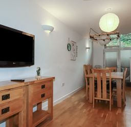 A dining room with a wooden table and chairs a wall mounted tv and glass doors at Tregullan in Porthtowan