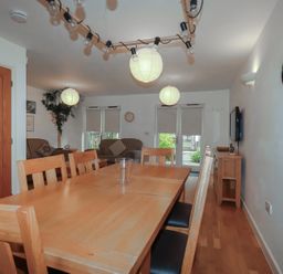 A dining table with wooden chairs in a room with sofas plants and wall art at Tregullan in Porthtowan