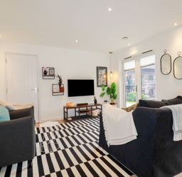 A living room with two sofas a striped rug a wall-mounted television and two mirrors at Treveglos in Porthtowan