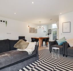 A living room with black sofas a striped rug and a wooden dining table with black chairs at Treveglos in Porthtowan