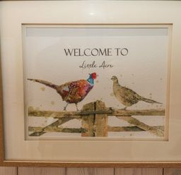 A framed picture of two birds on a wooden fence with the text welcome to Little Acre