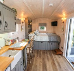 A compact room with a kitchenette on the left and a bed at the back with a small TV on the wall at Little Acre in Oxenhope