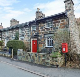 A stone cottage with a red front door and a red post box outside at Llety in Beddgelert