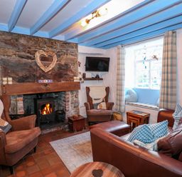 A living room with a stone fireplace and wood stove two armchairs a leather sofa and a window seat at Llety in Beddgelert