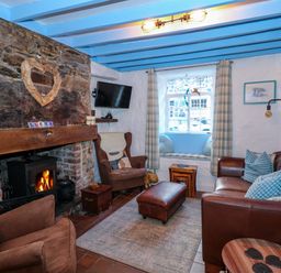 A living room with a stone fireplace and wood burning stove armchairs and a leather sofa at Llety in Beddgelert