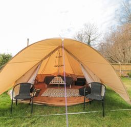 A bell tent with two chairs outside a bed and rug inside surrounded by grass and trees at Bell tent 2 Camerton near Timsbury