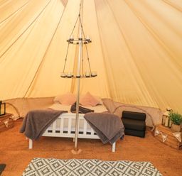 A bed with pillows and blankets inside a bell tent with wooden crates and a hanging candle holder at Bell tent 2 in Camerton near Timsbury