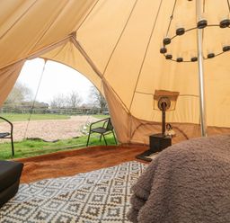 The interior of a bell tent with a wood stove a kettle a circular candle holder two chairs and outdoor view at Bell tent 2 in Camerton near Timsbury