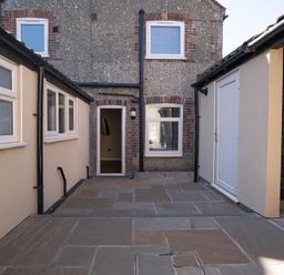 An outdoor patio area with stone flooring between buildings with windows and a door at Driftwood in Kessingland