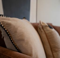 Two cushions on a brown sofa with a white wall in the background at Driftwood in Kessingland